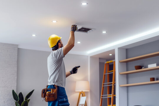 Electrician installing a new light fixture on the ceiling, with a toolbox and ladder in a modern living room.