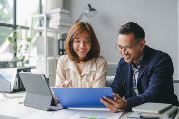 Two smiling asian businesspeople discussing work, looking at documents and using a digital tablet in a modern office