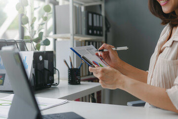 Businesswoman taking notes on a clipboard while examining financial charts at her desk in her office