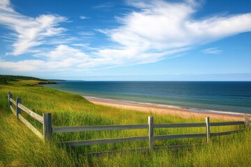 A scenic view of a grassy meadow with a wooden fence overlooking a serene beach and the ocean under a clear blue sky.