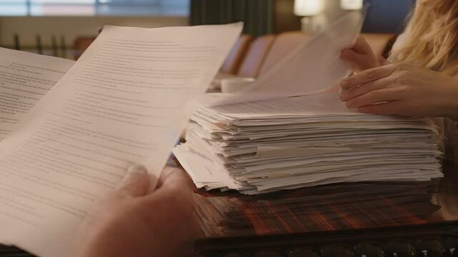 Close-up view of hands of two unrecognisable people working with stack of documents at conference table in law firm
