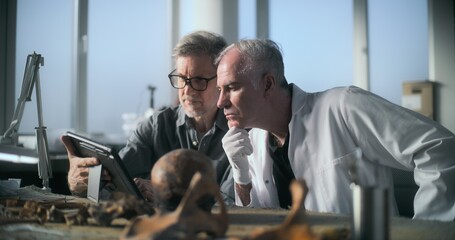 Archaeological laboratory: Mature archaeologist uses tablet computer and talks to senior...