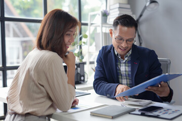 Two asian business people are reviewing financial data and discussing over documents in the office
