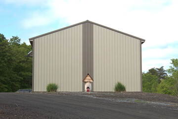 Side of an industrial building with a log statue in front that is shaped like a small house.  There are clumps of grass growing on each side of the building. 