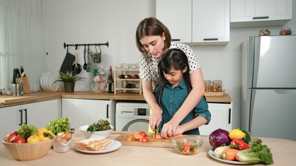 Smart caucasian mother and asian girl cooking together and chopping vegetable or preparing salad for dinner. Happy mom and daughter making healthy food with fresh food. Healthy food concept. Pedagogy.
