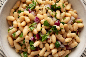 Homemade White Bean Salad with Herbs and Onion in a Bowl, top view. Flat lay, overhead, from above.