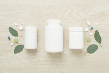 Bottles with pills and green leaves on wooden background, top view