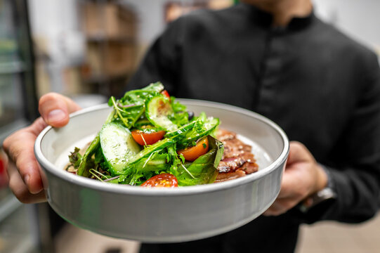 person holding a bowl of fresh salad with mixed greens, cherry tomatoes, and sliced cucumbers. The vibrant colors and healthy ingredients suggest a nutritious meal option