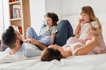 Obraz premium Happy family playing and laughing together on bed in the morning