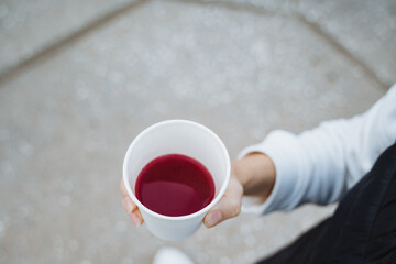 A person is firmly gripping a cup filled with a vibrant red liquid in their hand, creating an intriguing visual as they hold it steady against the backdrop of their surroundings