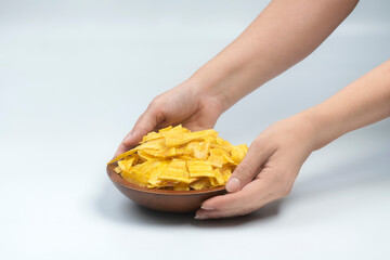 Studio shot of female hands picking Indian snack banana wafers from a shallow disposable cardboard...