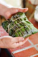 Manos de mujer adulta sosteniendo preparación tradicional latinoamericana en hoja de plátano