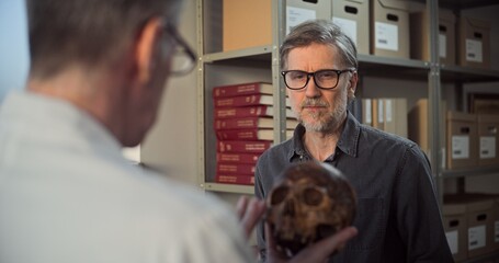 Two archaeologists analyze and examine skull of ancient extinct human, have discussion during...