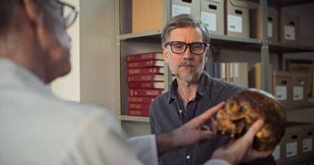 Two archaeologists analyze and examine skull of ancient extinct human, have discussion during...