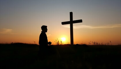 Silhouette of man kneeling near the wooden Christian cross on a nature meadow grass field outdoor at sunset