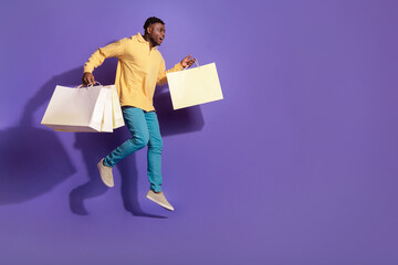 Full length photo of handsome young guy jump run shopping bags dressed stylish yellow garment isolated on violet color background