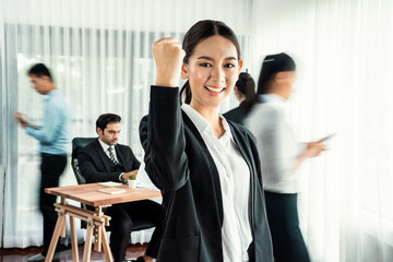 Portrait of happy young asian businesswoman looking at camera, raise her celebrate fist with motion blur background of business people movement in dynamic business meeting. Habiliment