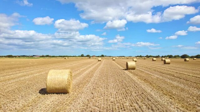 In an aerial view, we are treated to the sight of wind turbines gracefully turning in a Lincolnshire farmer's just-harvested field, with golden hay bales creating a picturesque foreground.
