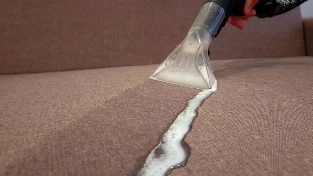 Cleaning fabric upholstery with a powerful vacuum cleaner in a cozy living room