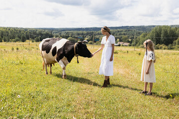 mother daughter in the meadow and looks and strokes the cow, summer in the village