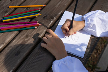 Obraz premium preschool girl drawing with colored pencils outdoors, development of creativity