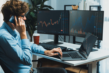 Young investor stock trader discussing on smartphone to broker, looking on dynamic financial exchange investment on screen at back side in current market graph in real time at modern office. Gusher.