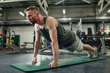 Fototapeta premium Shredded man dressed in gray sportswear standing in straight arm plank after main workout