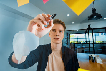 Professional caucasian businessman writing marketing idea by using mind map and sticky notes on glass board at modern meeting room. Creative business and planing concept. Closeup. Immaculate.