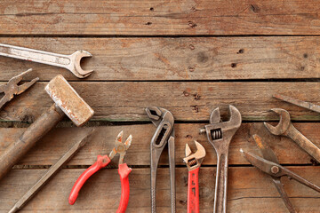 Old hand tools on a wooden surface, top view. Adjustable wrench, hammer, sledgehammer, tin snips and pliers. Tools for repair and construction. Wooden floor and tools