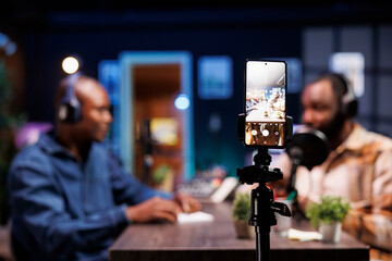 Selective focus of a smartphone on tripod being used to record two african american bloggers...