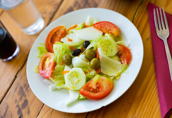 Plate of colorful appetizing salad of fresh greens, slices of cucumber, tomato and onion, topped with piquant pickled olives. Healthy light appetizer concept..