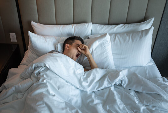 Sleepless man lying in bed waking up tired yawning suffering from insomnia 