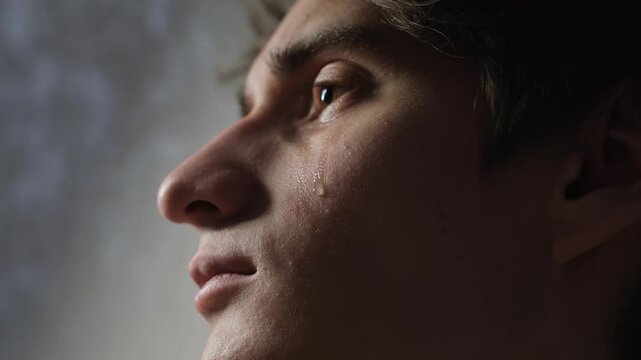 A tear rolls down the cheek of a young man, close-up