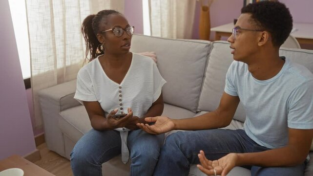 Mother scolding teenage son in living room setting while holding phone both wearing casual clothes sitting on couch