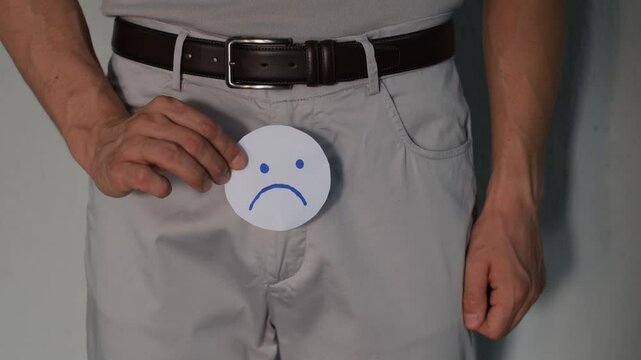 Prostatitis and prostate cancer concept. Problems with erection and urination. A man shows a sad smiley face on paper near the zipper of his pants
