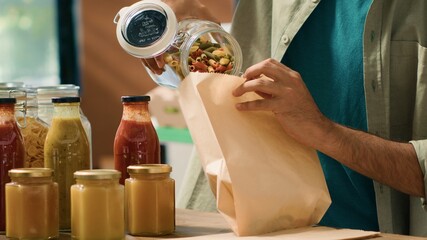 Adding pasta in paper bag to buy enough for nutritious supper, choosing organic pantry supplies from bulk products in recyclable containers. Customer goes shopping for food items. Handheld shot.