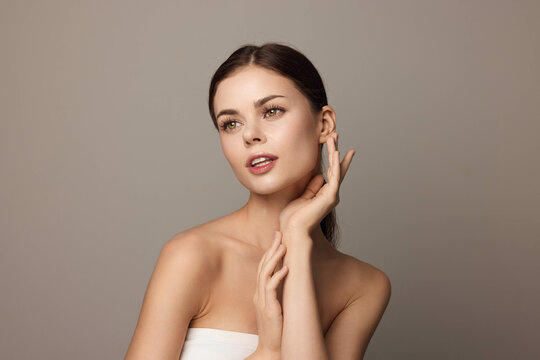 Beautiful young woman with hands on face, gray background, skin care and beauty concept