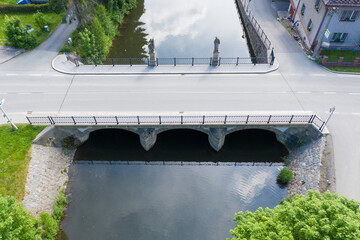 Sunny day at the stone arch Bridge. Scenic view of  road bridge from above. View under an old stone bridge on a flowing river. The river banks are overgrown with vegetation.