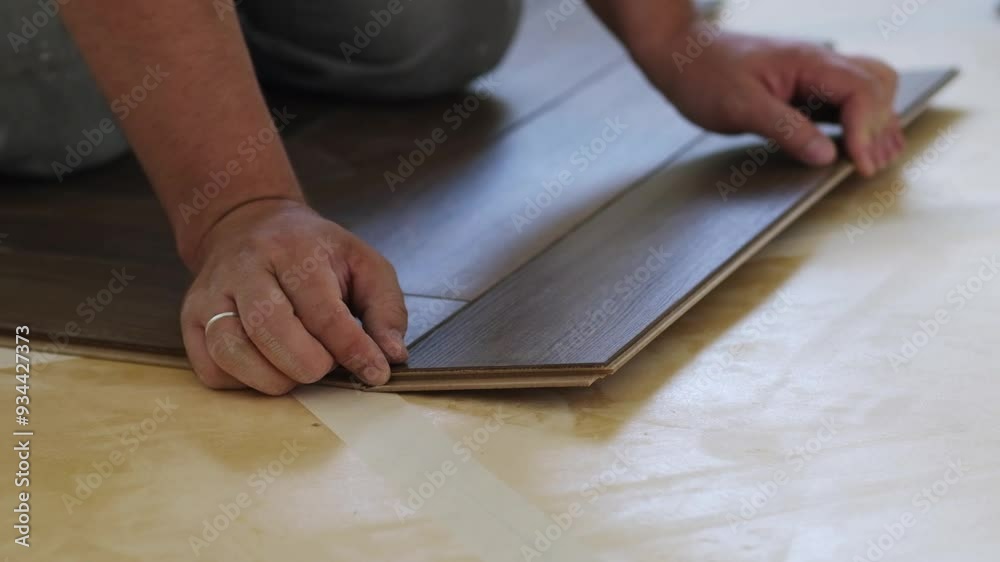Poster Close-up of a man kneeling and installing laminate flooring in a home.