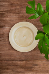 empty plate mock up on brown texture wooden background with monstera leaves