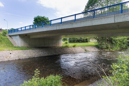 Reinforced concrete road bridge over the river. Close-up during sunny day in summer. Aerial view on a bridge across a small river. Canal or ditch with green grass meadow, Underneath of classic style 