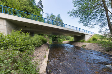 Reinforced concrete road bridge over the river. Close-up during sunny day in summer. Aerial view on a bridge across a small river. Canal or ditch with green grass meadow, Underneath of classic style 