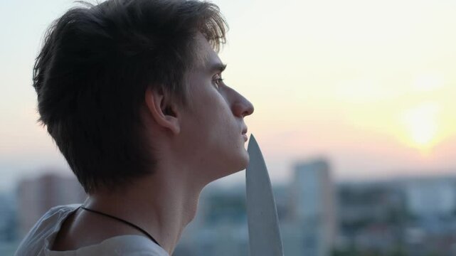 Strange pensive young guy with a knife at sunset, close-up