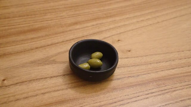 Closeup view of a man caucasian hand placing green olives in a black bowl on the wooden table