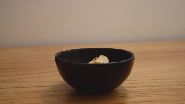Closeup view of a man caucasian hand placing chips  in a black bowl on the wooden table