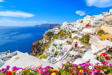 The blue dome church, whitewashed village and blue Aegean Sea are visible from a terrace with flowers in the town of Oia on the island of Santorini Greece.