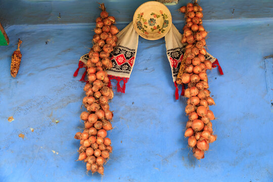 Europe, Romania. Onions drying on side of house next to pottery and embroidery.