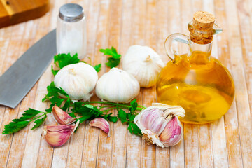There is knife, garlic, fresh parsley and carafe of olive oil on cutting board. Fragrant...