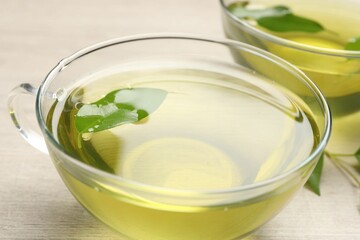 Refreshing green tea in cups and leaves on wooden table, closeup