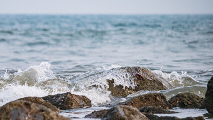 Waves splashing over rocks in sea beach shore. White surf and blue sea. 